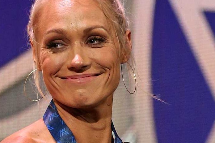 Standing in front of a giant replica of the medal, Erin Phillips wears the real one, holds some champagne and smiles