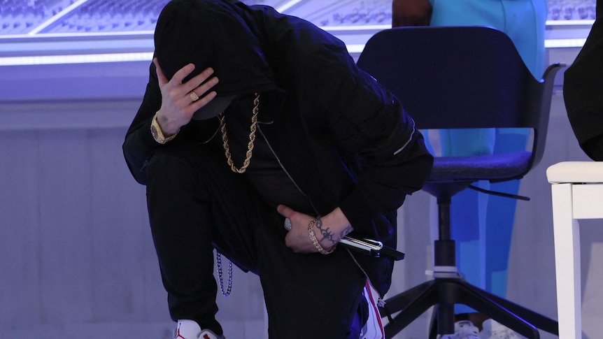 Eminem on his knee wearing black with hand on head