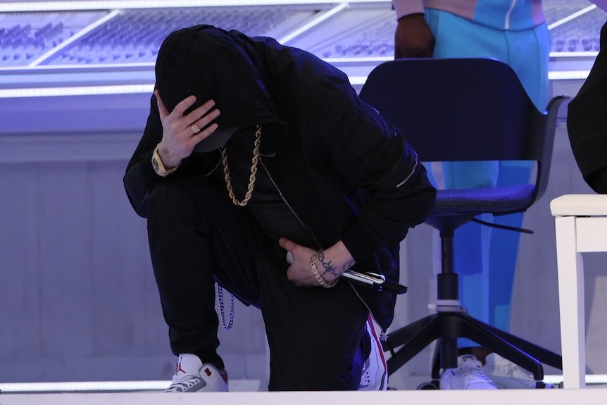 Eminem on his knee wearing black with hand on head