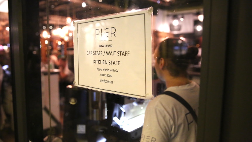 a workers stands next to a sign in a restaurant window advertising job vacancies