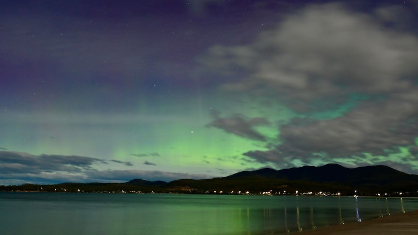 An aurora glows over a calm body of water.