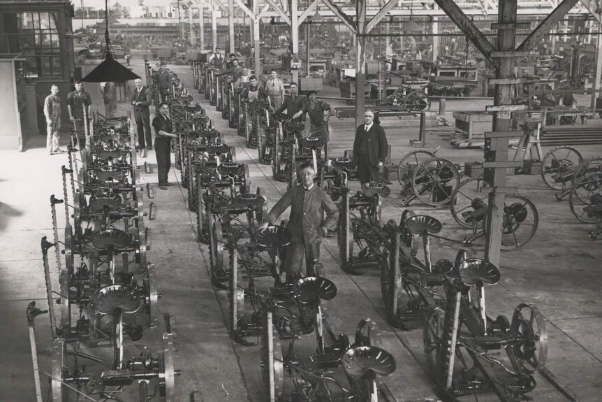 Black and White photo of a factory floor with rows of old-fashioned mowers.