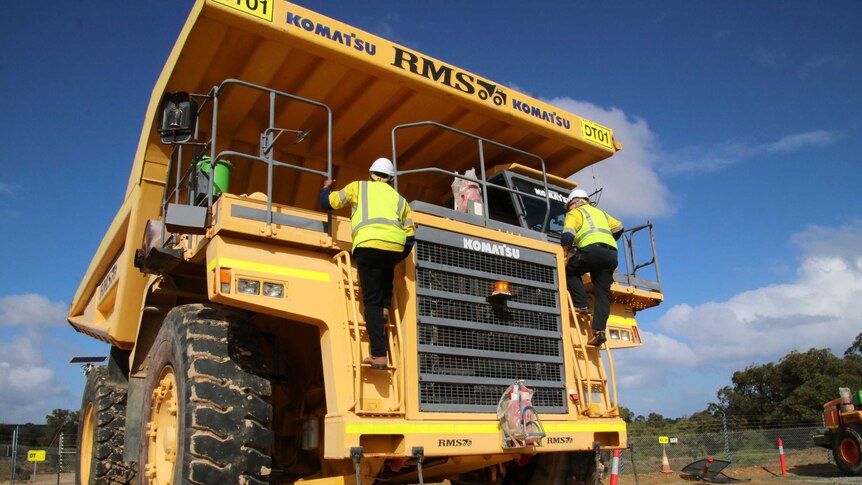 A 100-tonne payload capacity dump truck with workers standing on the front of it.