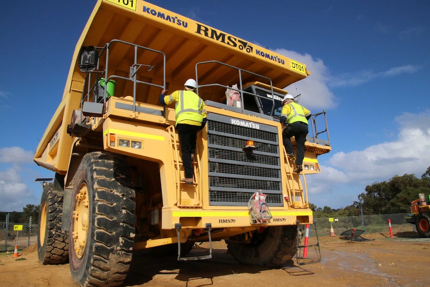 A 100-tonne payload capacity dump truck with workers standing on the front of it.