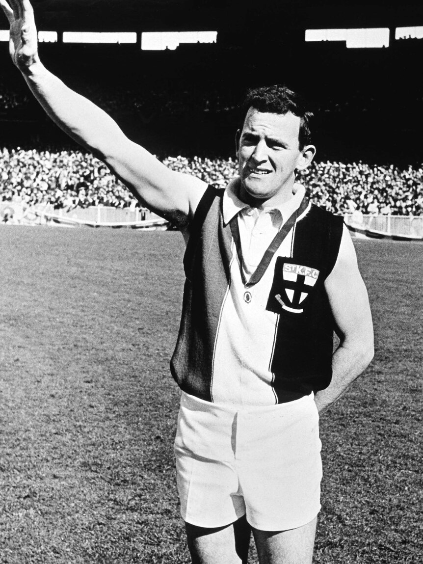 A black and white photo of an AFL footballer waving on-field.