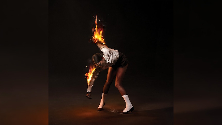 St. Vincent dances wearing black and white, her arms set alight on fire, against a dark background