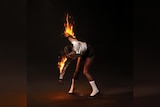 St. Vincent dances wearing black and white, her arms set alight on fire, against a dark background