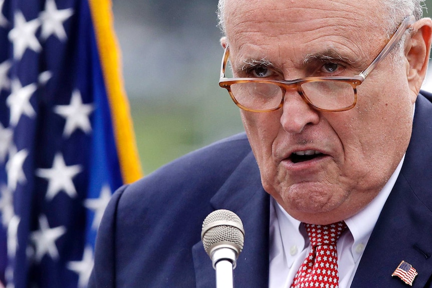 Rudy Giuliani close-up, he talks in front of a mic with a serious look on his face.