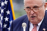 Rudy Giuliani close-up, he talks in front of a mic with a serious look on his face.