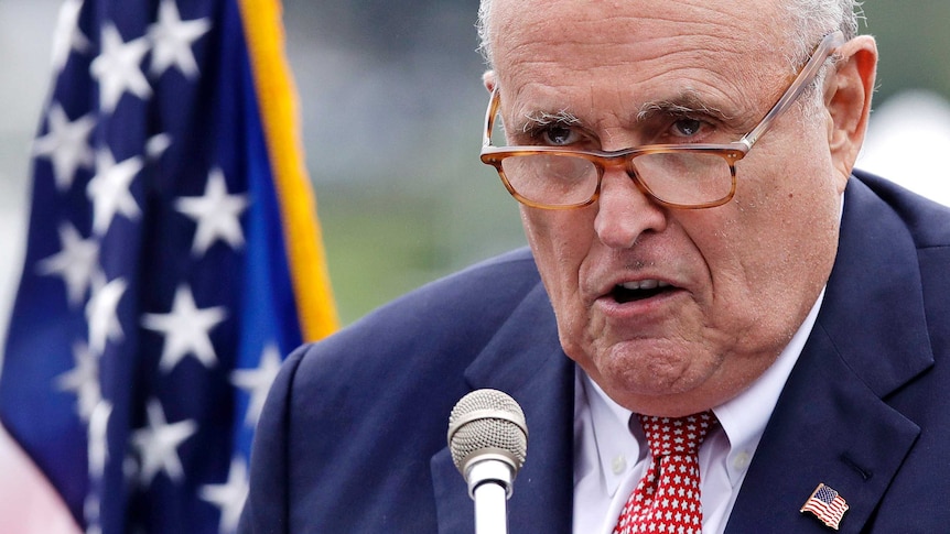 Rudy Giuliani close-up, he talks in front of a mic with a serious look on his face.