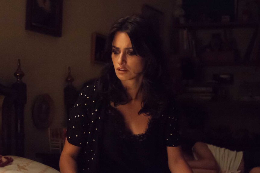 Film still featuring actress  Penélope Cruz with a distressed look on her face and she sits on a bed.