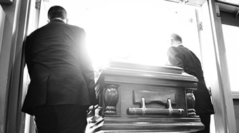 Men carry a coffin through a doorway.