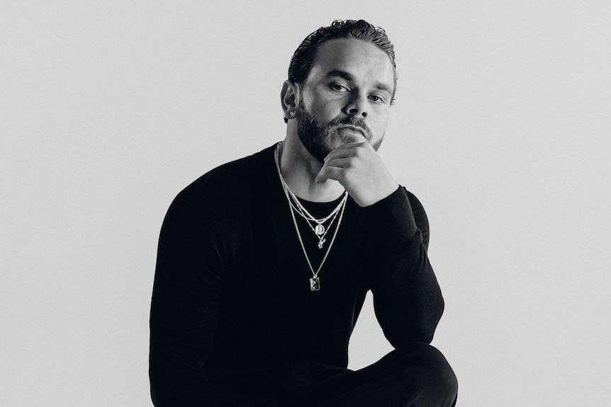 Man wearing a black shirt and necklaces looks to camera