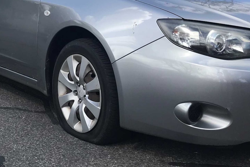 a grey car with a flat front tyre