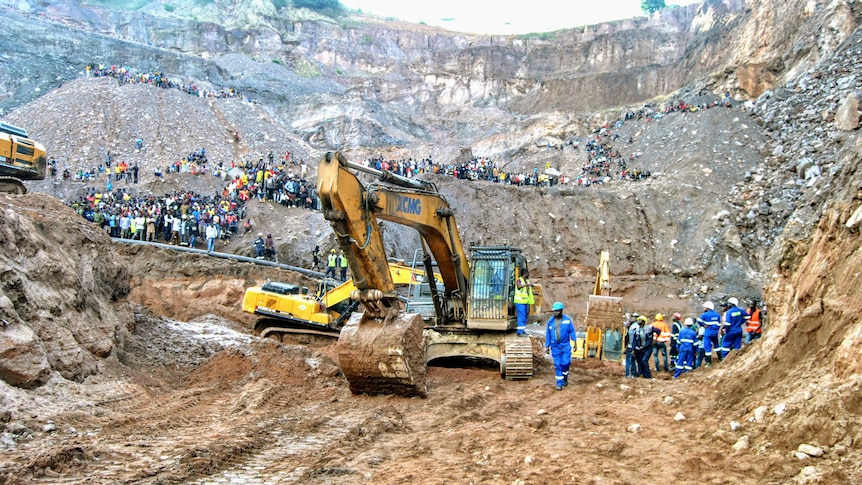 An excavator on a mine with many people standing around. 