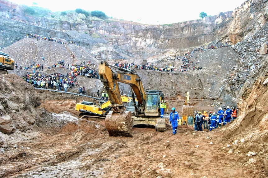 An excavator on a mine with many people standing around. 