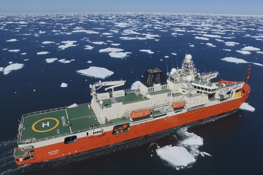 A red ship moves through broken up sea ice.