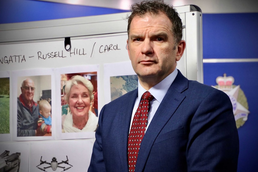 Detective Inspector Andrew Stamper stands in front of a white board with photos of Russell Hill and Carol Clay and maps.