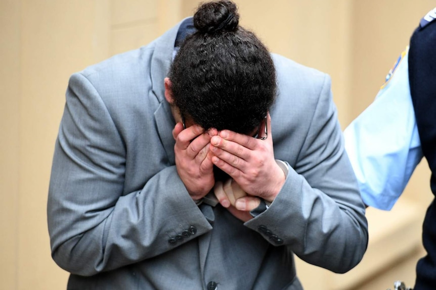 A man covers his face, as he is held by a corrections officer.