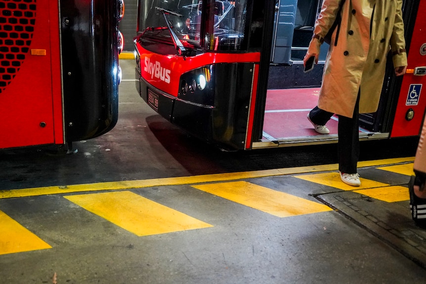 A person wearing a trenchcoat is stepping of an idling skybus