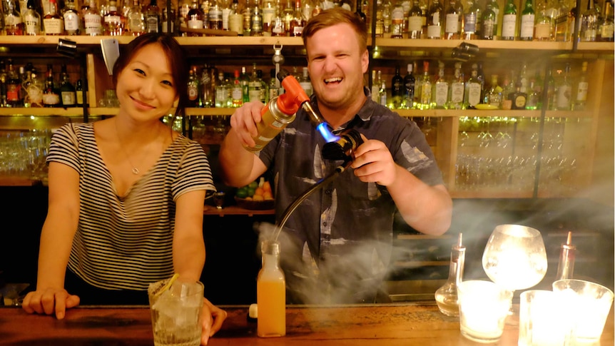 A woman at a bar with a man making a cocktail