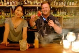 A woman at a bar with a man making a cocktail