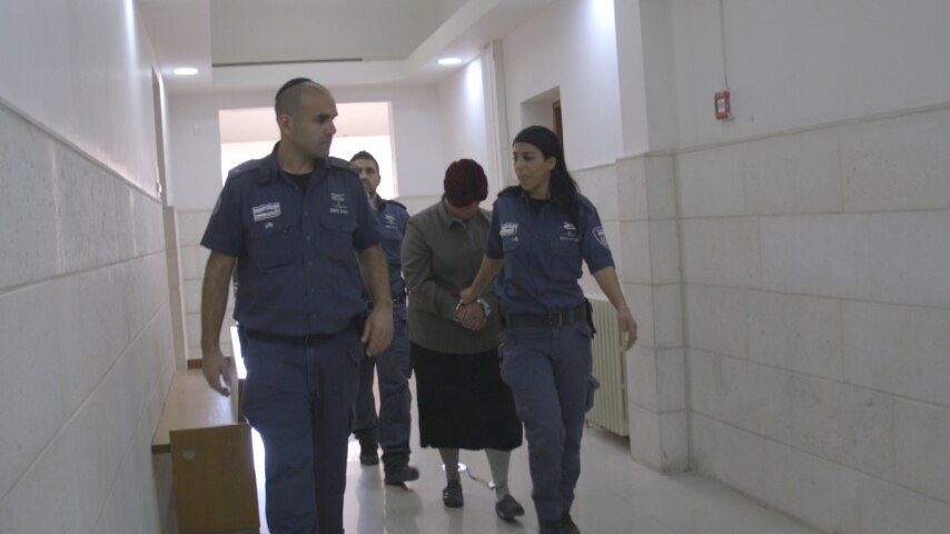 Malka Leifer hangs her head as she is walked down a hallway by police officers.