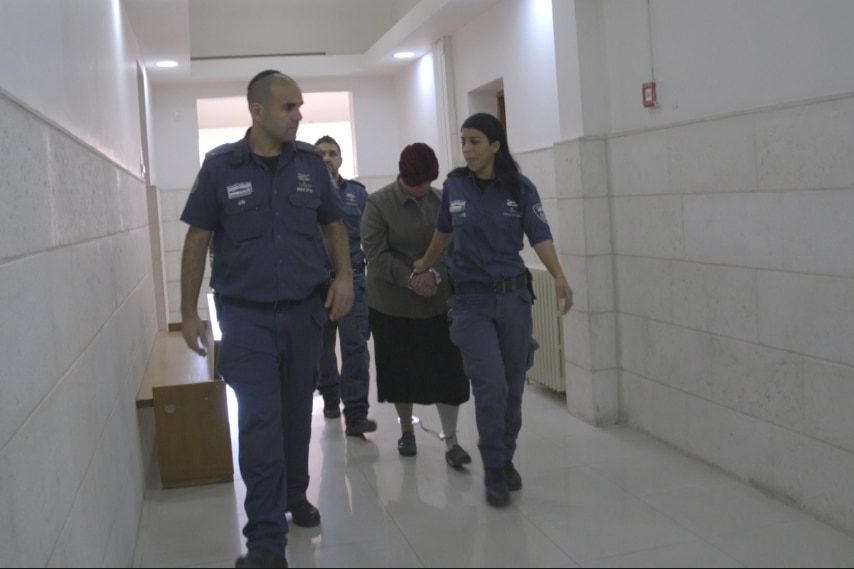Malka Leifer hangs her head as she is walked down a hallway by police officers.
