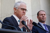Malcolm Turnbull gestures with both hands, Josh Frdyenberg stands behind him.