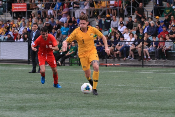 A footballer in a yellow kit running with a football at his feet.