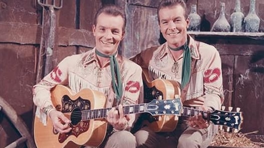 identicle twins are in cowboy gear holding guitars