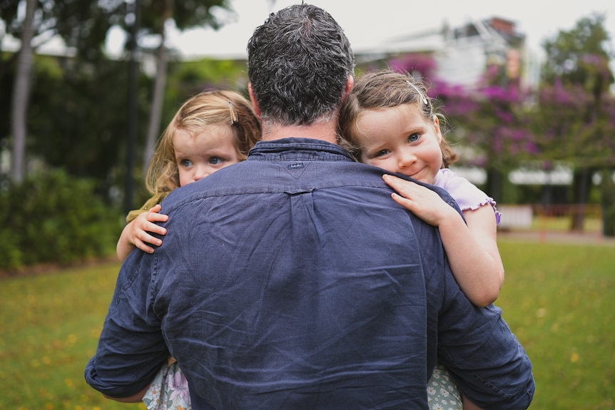 Two girls look over the shoulder of their dad.