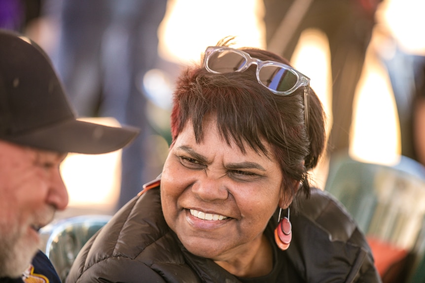 A woman with sunnies on her head laughs while talking to a man. 