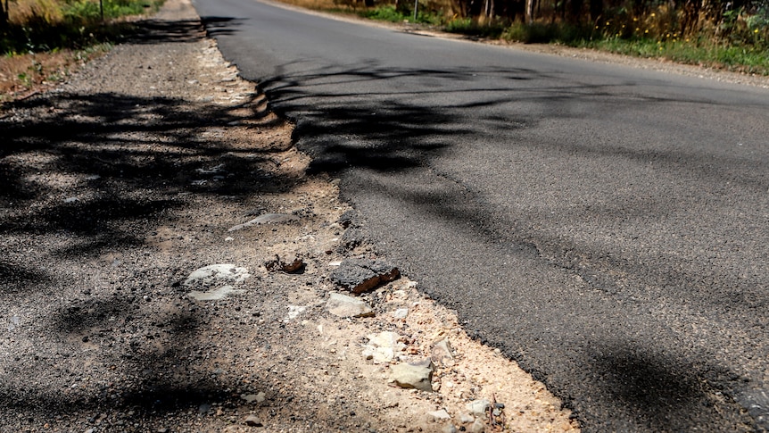 Cracked road edge with asphalt breaking into gravel road shoulder