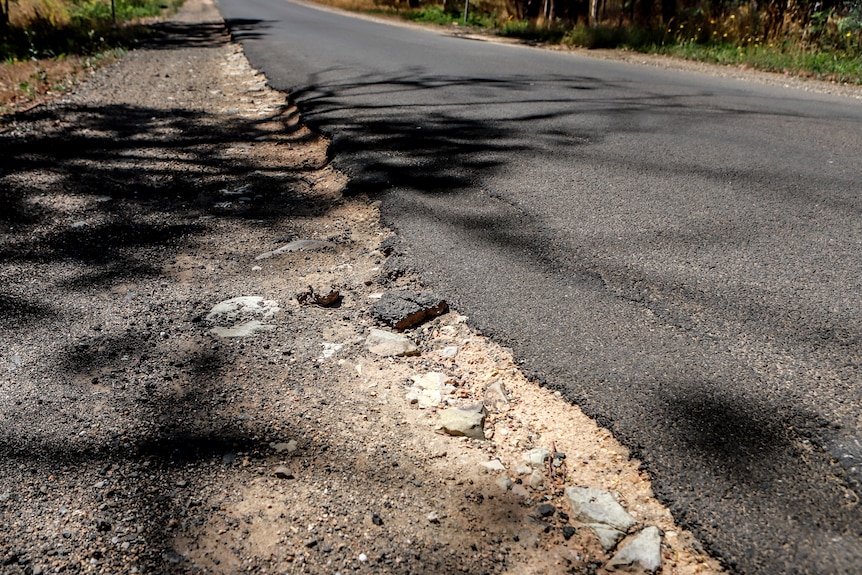 Cracked road edge with asphalt breaking into gravel road shoulder