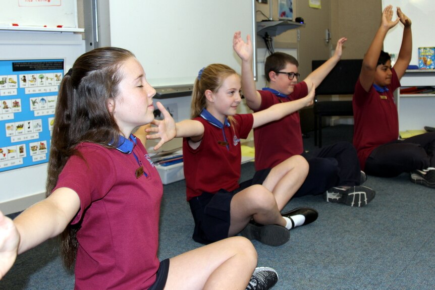 Four year six students sit on a classroom floor practising mindfulness, with arms stretched out, as part of a mindfulness class.