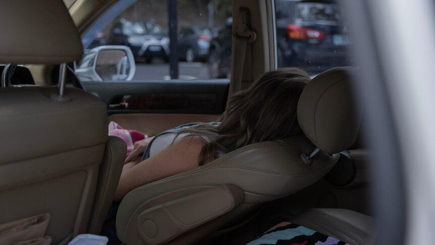 A woman laying down in a car.