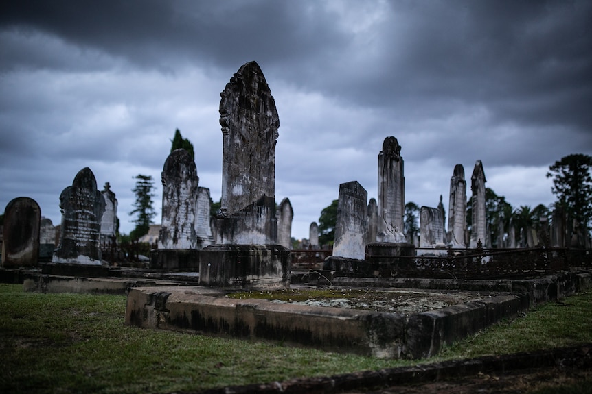 Large headstones in various states of disrepair against a stormy grey sky.
