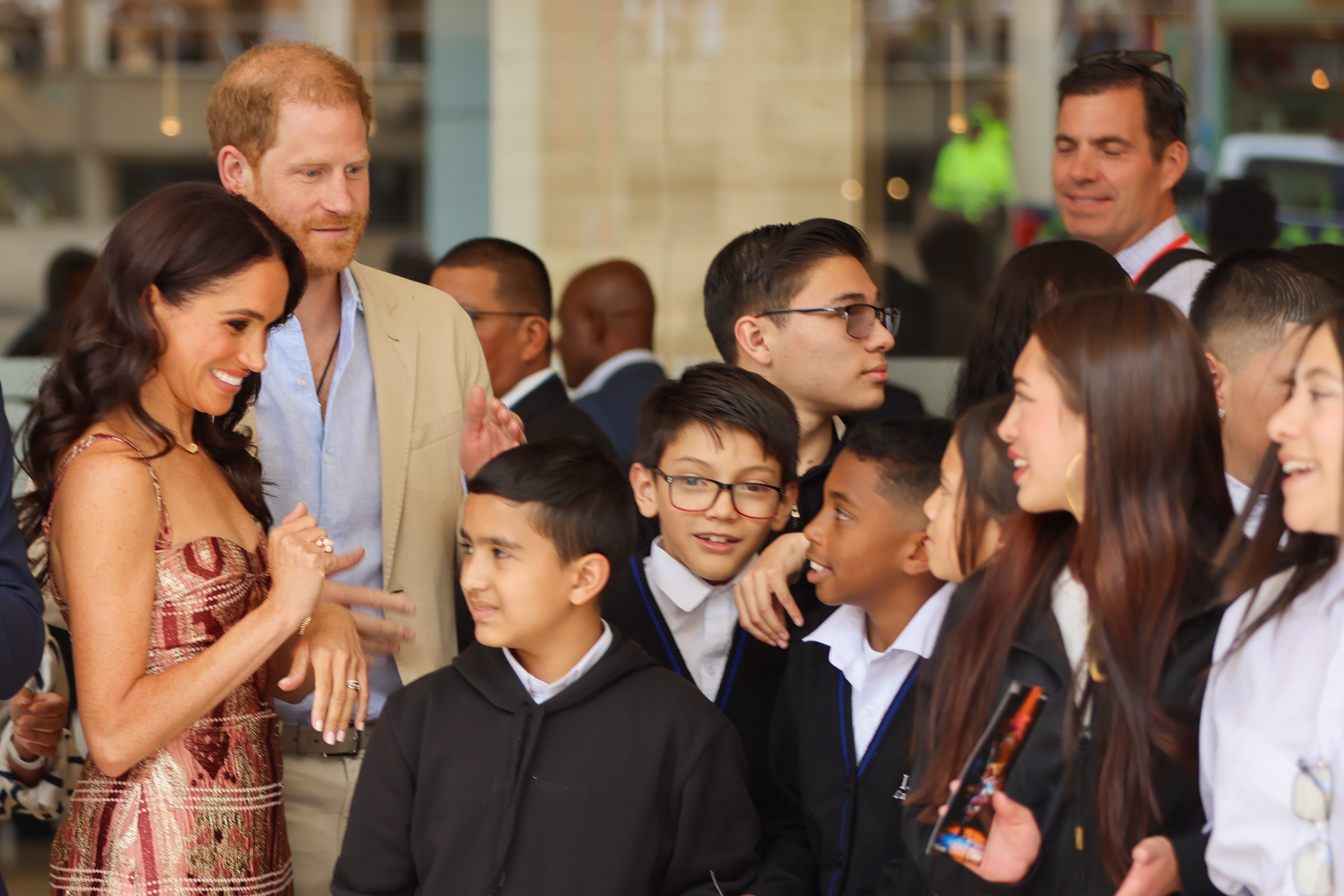 Meghan and Harry smile as they talk to a crowd of teenaged students during an event.