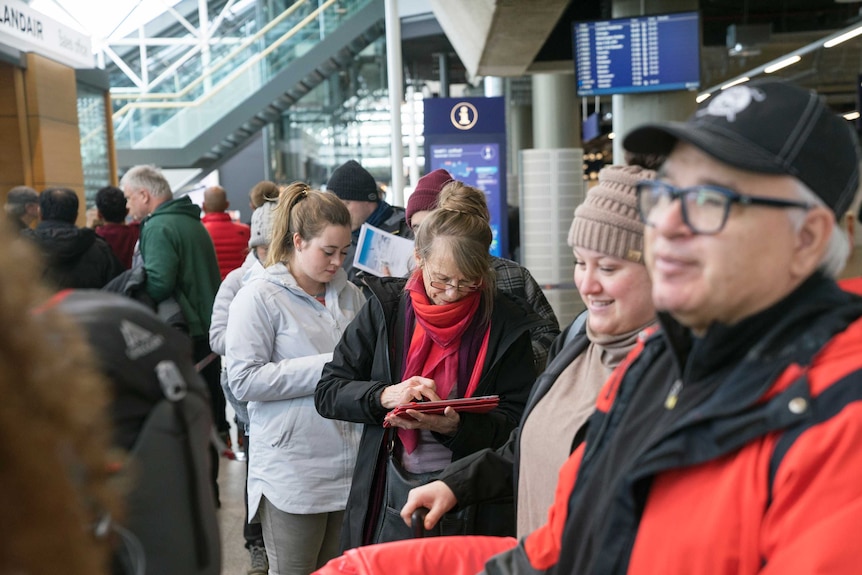 About a dozen people, dressed in winter clothes, standard inside an airport