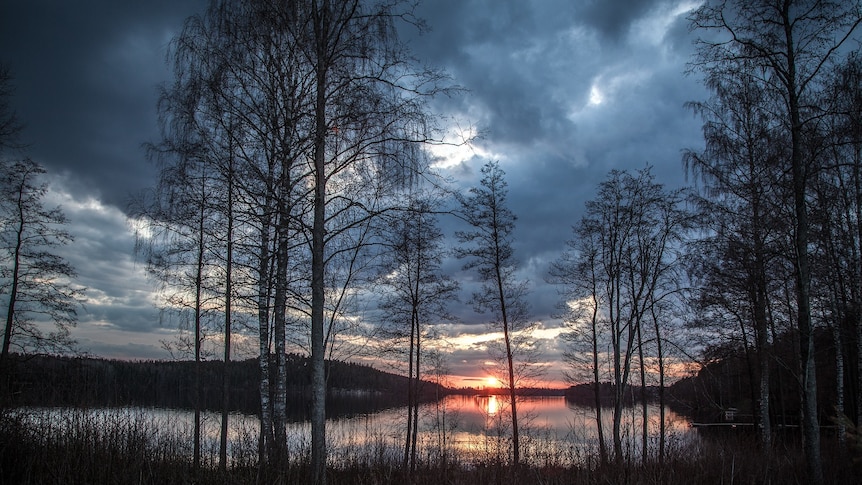 A setting sun through a brooding sky over a lake in Finland. (Image by Kerttu from Pixabay)