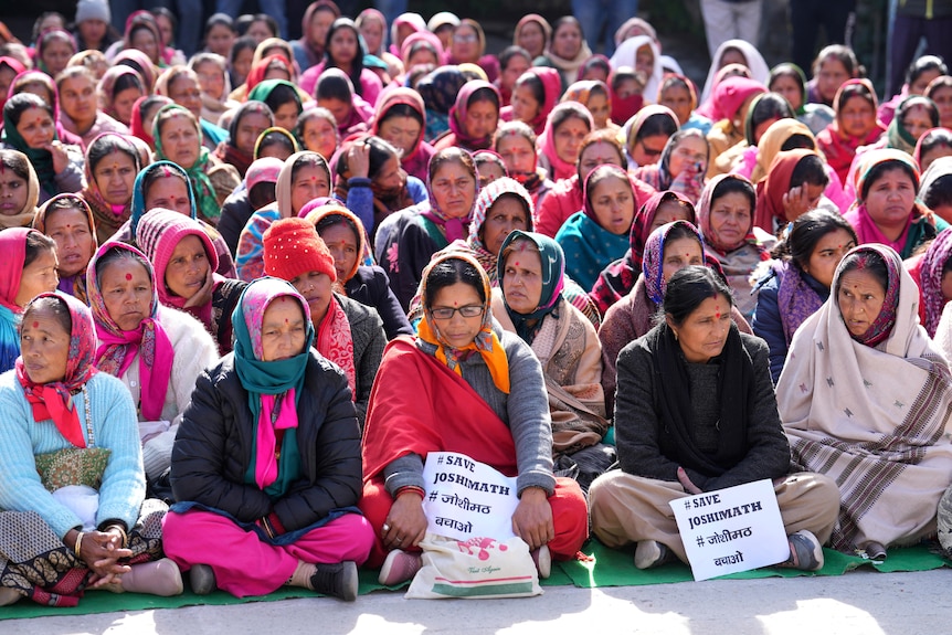 A group of women sit in rows on the ground with some holding signs.