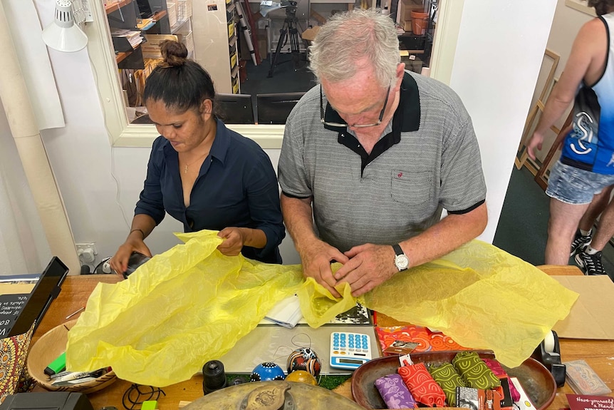 Kimberly and Pete sit at a desk and wrap toys.