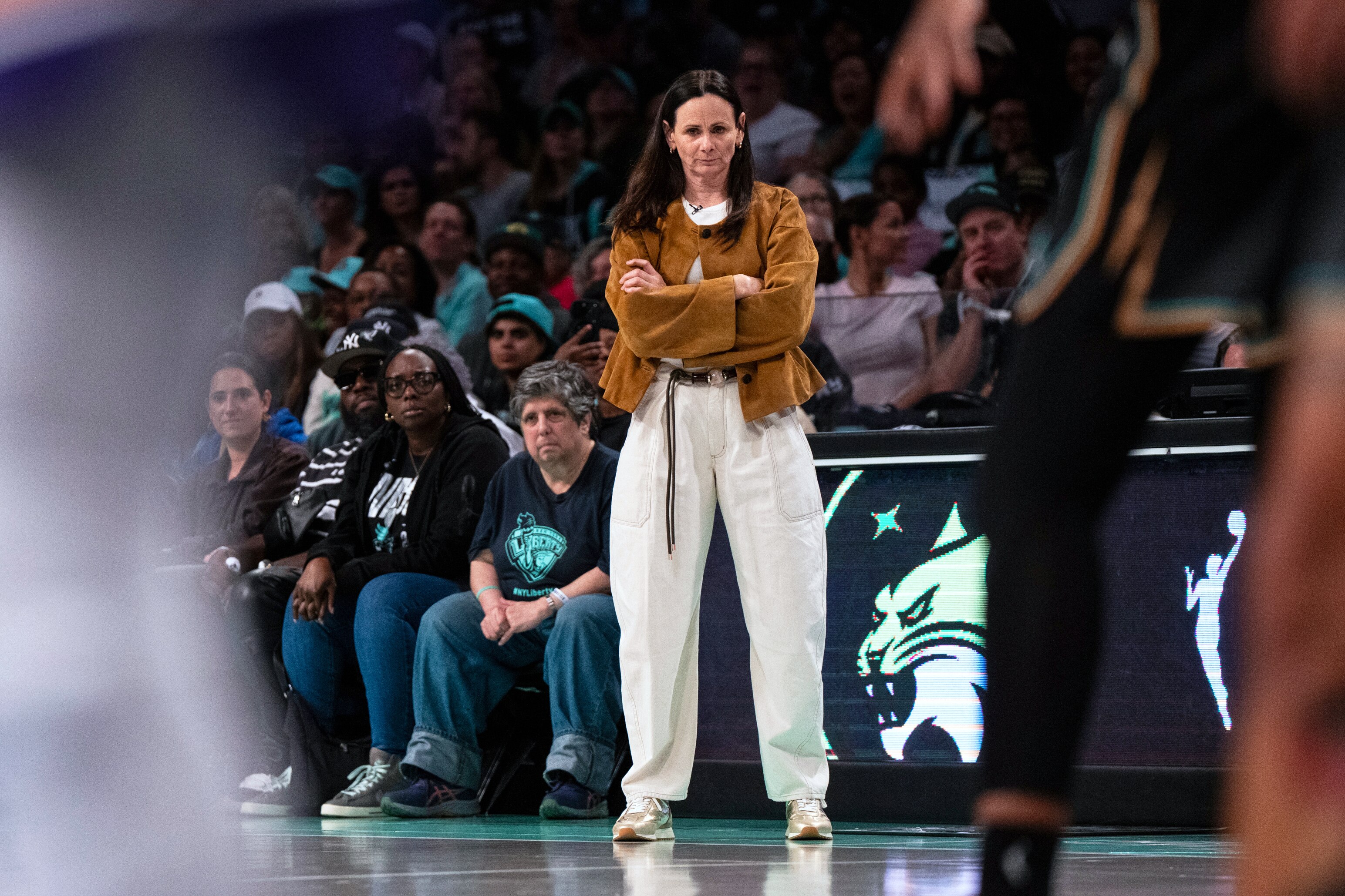 Female basketball coach stands courtside watching the game, arms folded