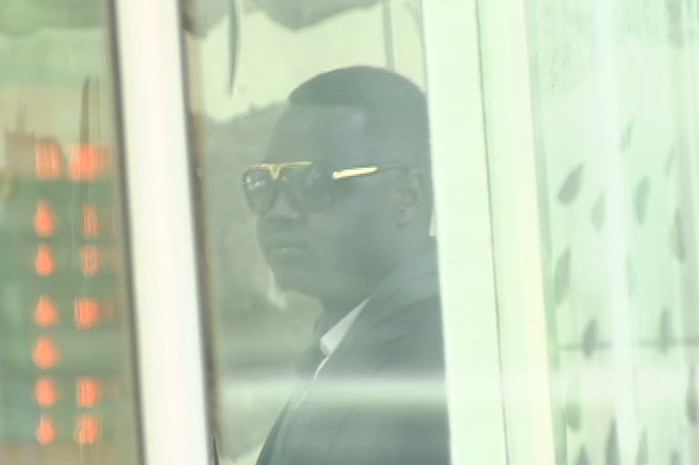 Kuol Deng is seen through a window as he leaves the County Court building in Melbourne.