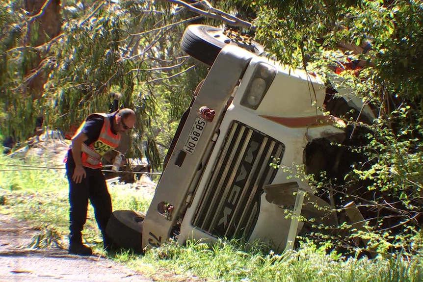 A police officer looks at a truck on its side