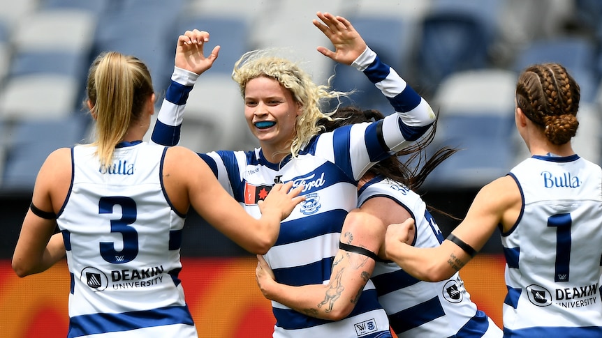 A Geelong AFLW player smiles as she puts her hands up for a high-five with teammates after a goal.