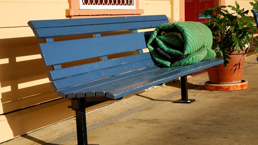 A green swag or bed roll, wrapped on a bench on a platform
