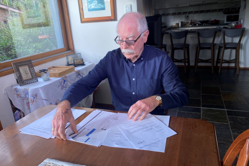 A man in his seventies sits at his kitchen table and looks at banks documents 