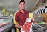 Butcher holds a tray of rib eye beef cuts.